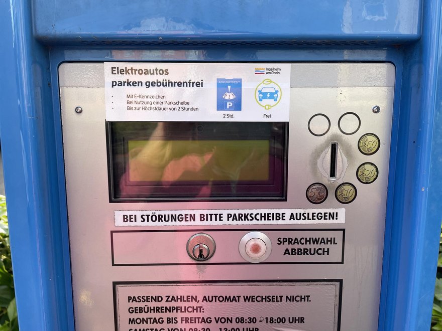 Ein Parkscheinautomat mit einem Aufkleber der Stadt Ingelheim. Der Text auf dem Aufkleber ist, Elektroautos parken gebührenfrei, mit E-Kenzzeichen, bei Nutzung einer Parkscheibe, bis zur Höchstdauer von 2 Stunden.